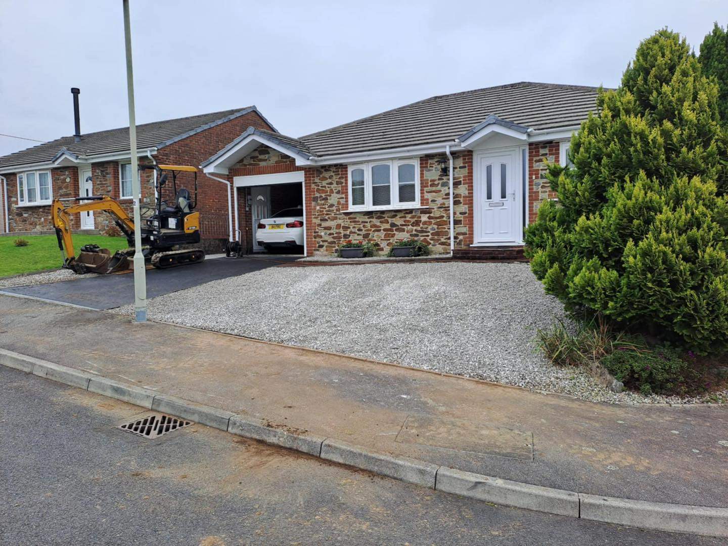 New gravel driveway mid-build — mini-digger in carport, bungalow front