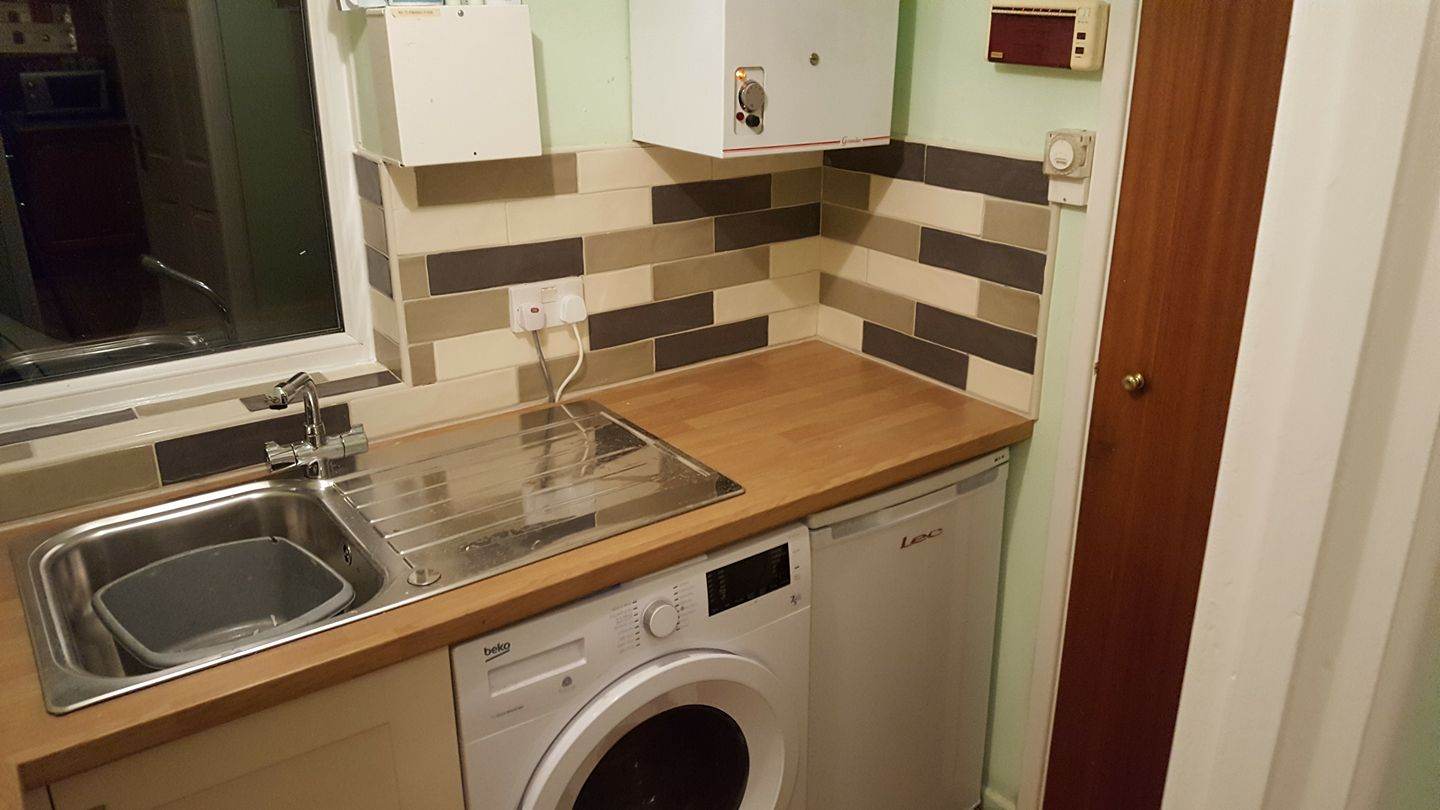 Completed utility room fit — oak worktop, stainless sink, Beko washer, brick-pattern splashback